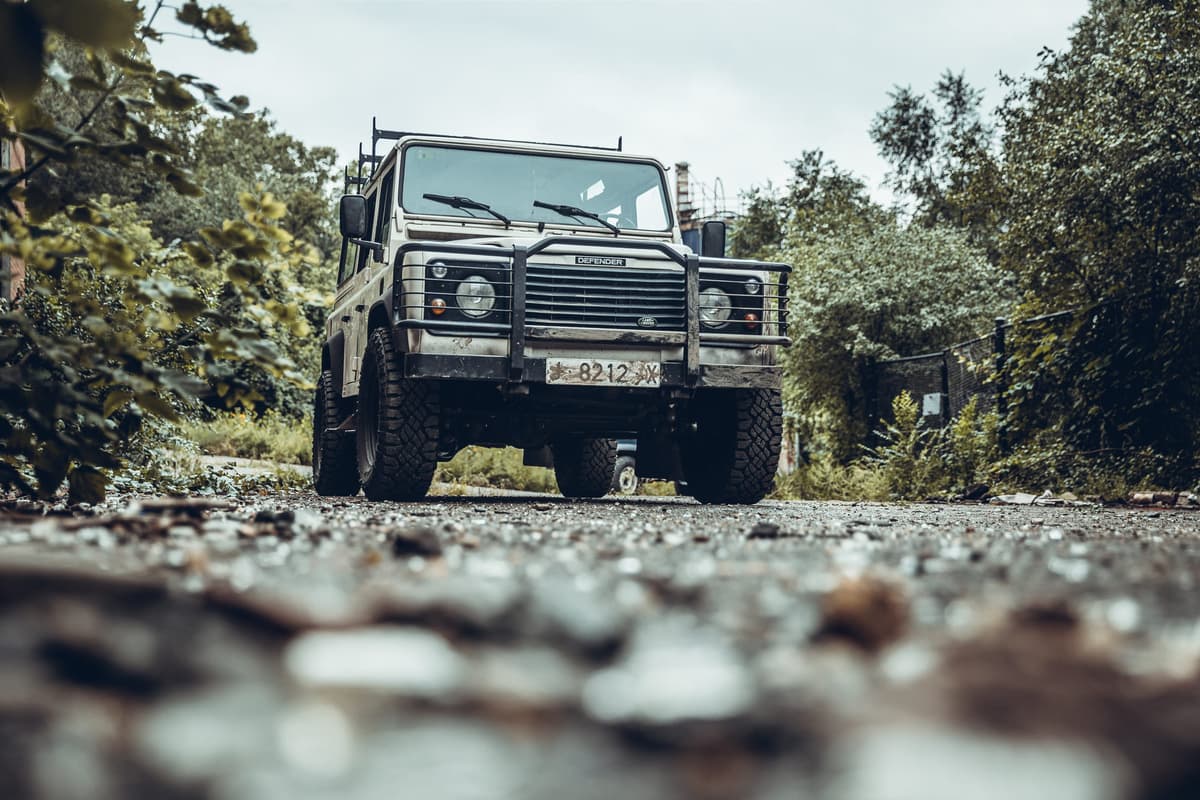 A weathered Defender 110 photographed low to the ground on a wet forest road