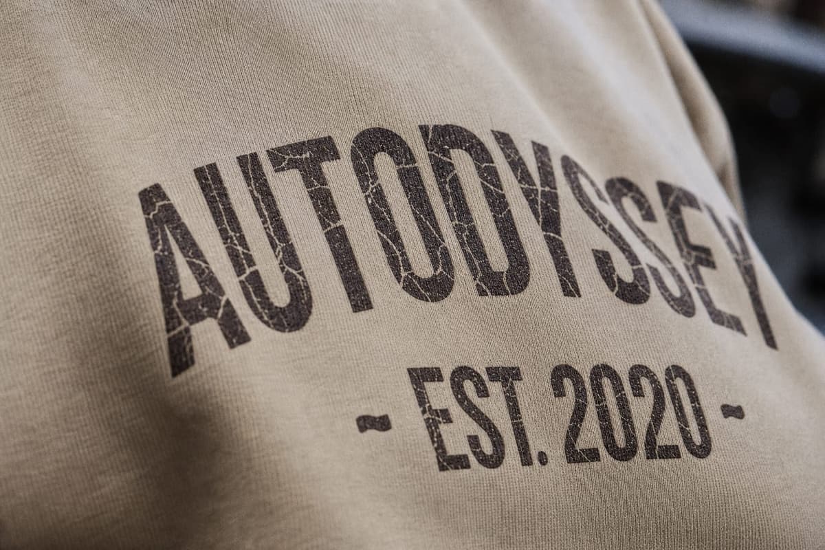 A close-up of the distressed AUTODYSSEY collegiate print on sand cotton